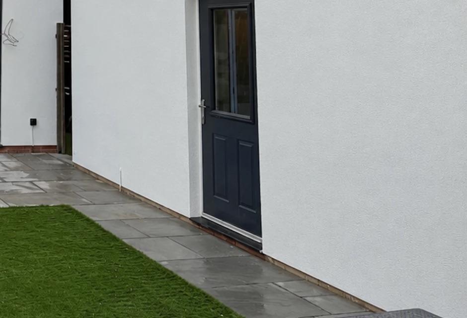Grey stone paving and lawn beside a freshly rendered garden outbuilding